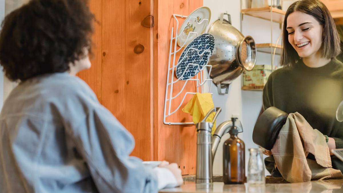 Cheerful young women speaking with each other and smiling in kitchen with different utensil